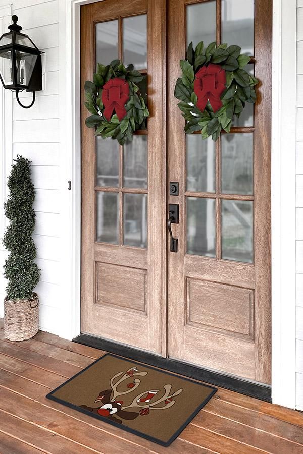 two wreaths sitting on the front door of a white house with wood flooring