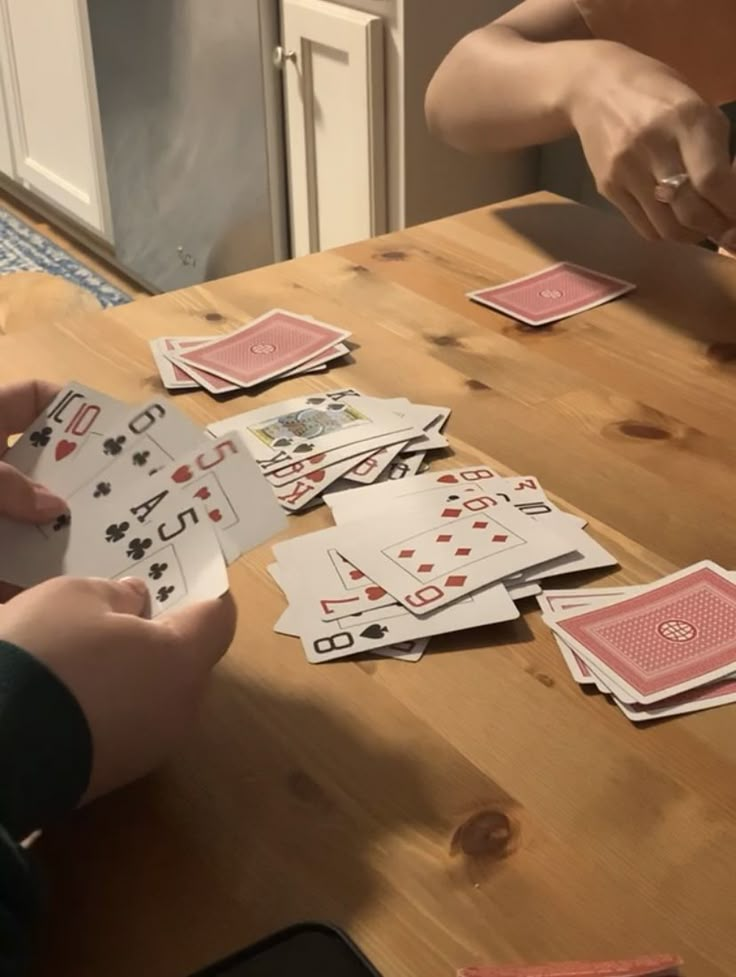 two people playing cards on a wooden table