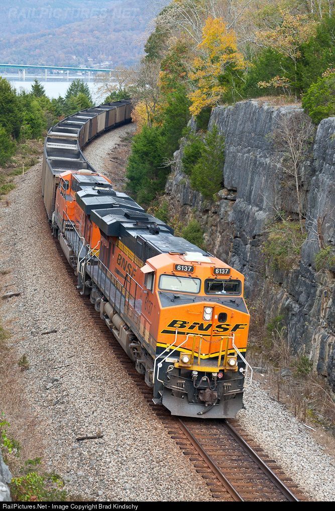 an orange and black train traveling down tracks next to a rocky mountain side with trees