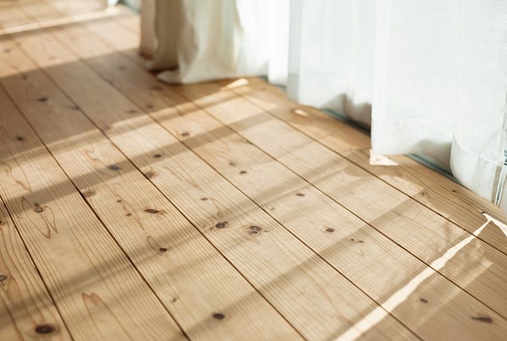 an empty room with wooden floors and white curtains on the windowsill, sunlight shining through