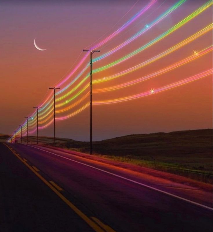 a long line of street lights on the side of a road at night with colorful streaks in the sky