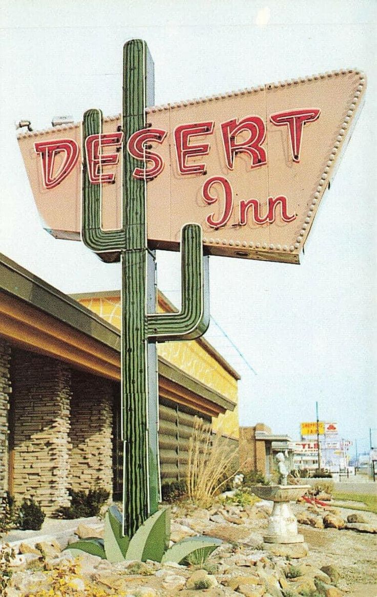 a desert sign with a cactus in the foreground and a building on the other side