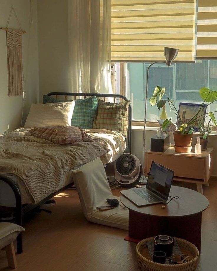 a bedroom with a bed, desk and laptop on the floor in front of a window