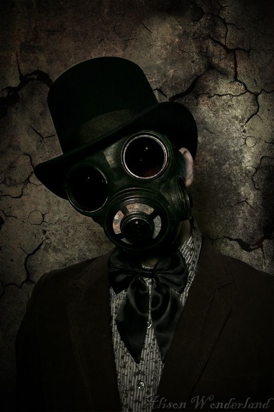 a man wearing a gas mask with a top hat and bow tie in front of a cracked wall