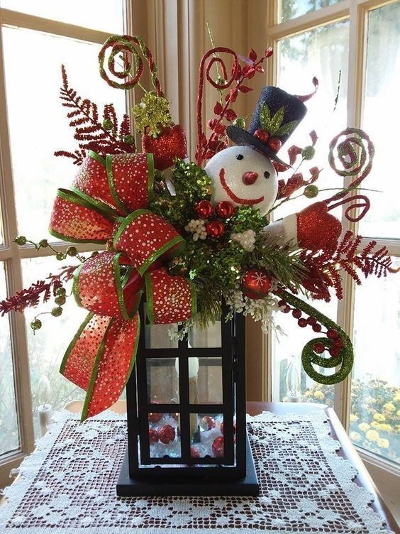 a christmas centerpiece with a snowman in a lantern on a table next to a window