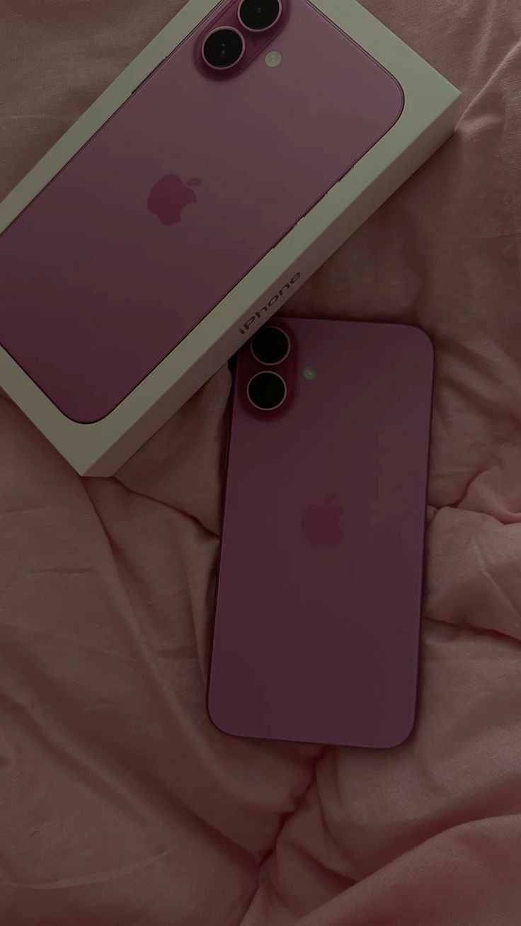 two purple iphones sitting on top of a pink bed next to an apple box