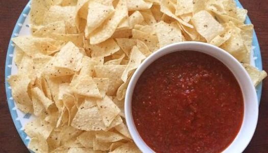 a bowl of salsa and chips on a blue and white plate with a wooden table