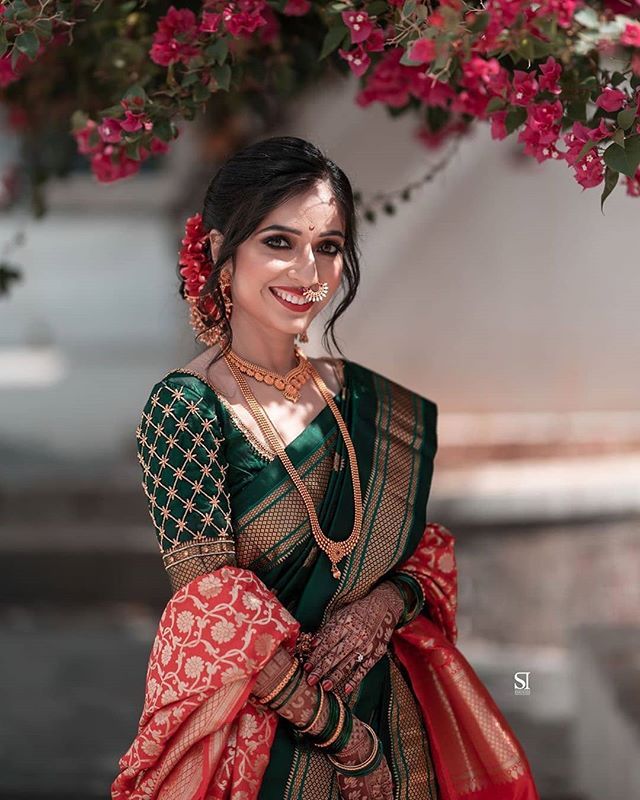 a woman wearing a green and red sari with flowers in her hair, smiling at the camera