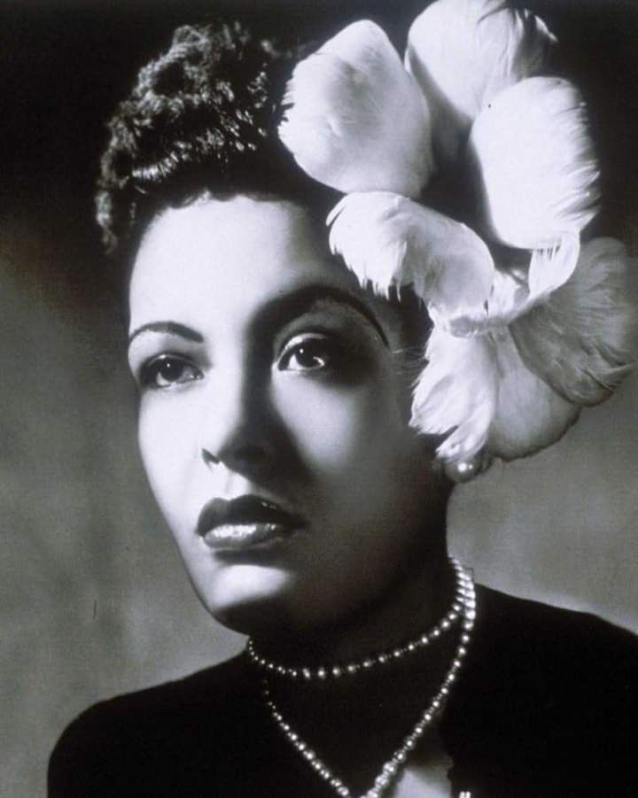 a black and white photo of a woman with flowers in her hair, wearing pearls