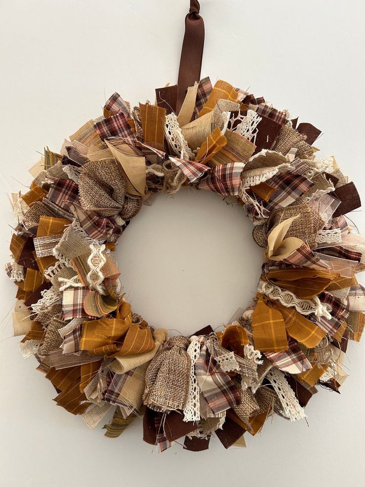 a wreath made out of fabric and burlocks hanging on a wall next to a brown ribbon