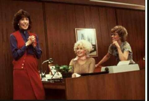 three women standing in front of a desk talking to each other and smiling at the camera