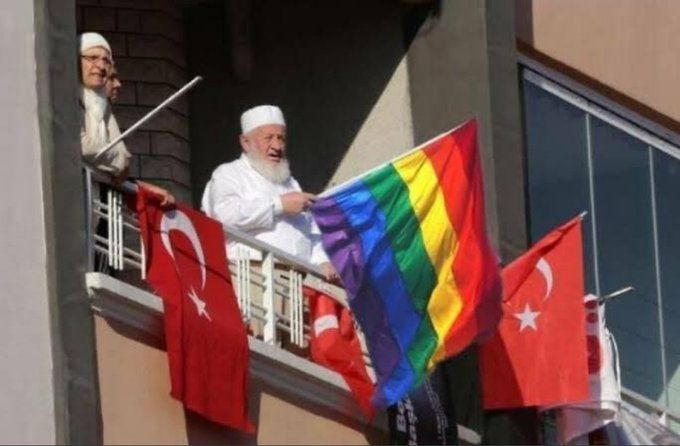 two men standing on a balcony holding flags and looking out the window at another man