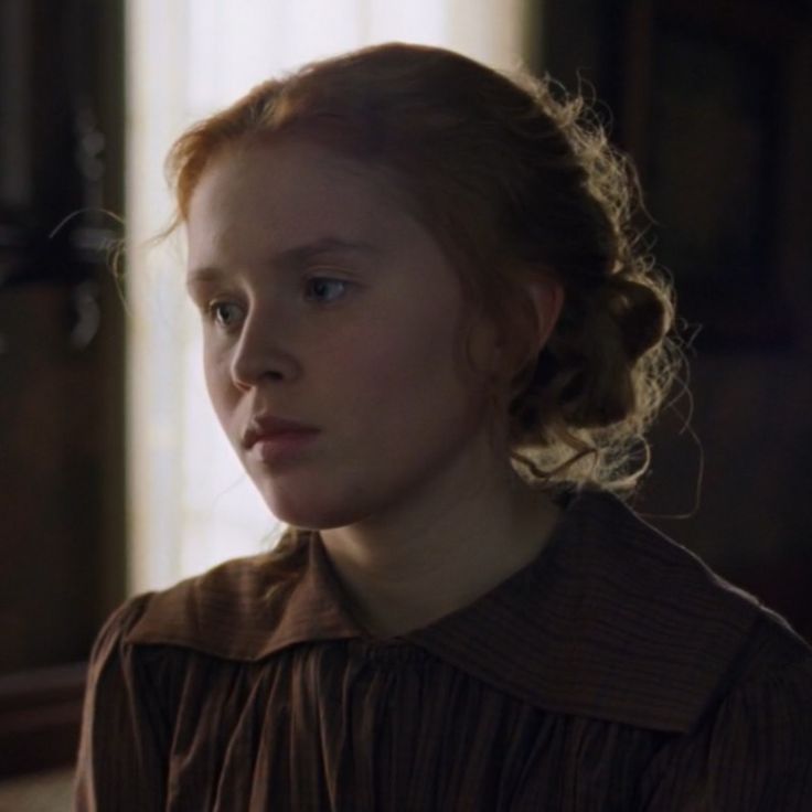 a woman with red hair and blue eyes stares into the distance in a dark room