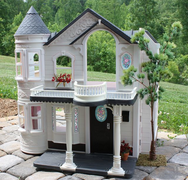 a doll house is shown in the middle of a stone patio with potted plants