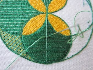 a close up of a piece of embroidery on a white cloth with green and yellow designs