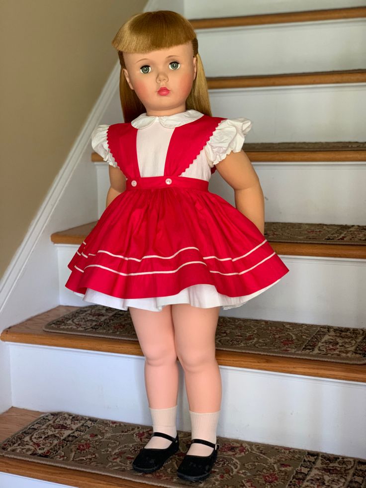 a doll is standing on the stairs with her hands in her pockets and wearing a red dress