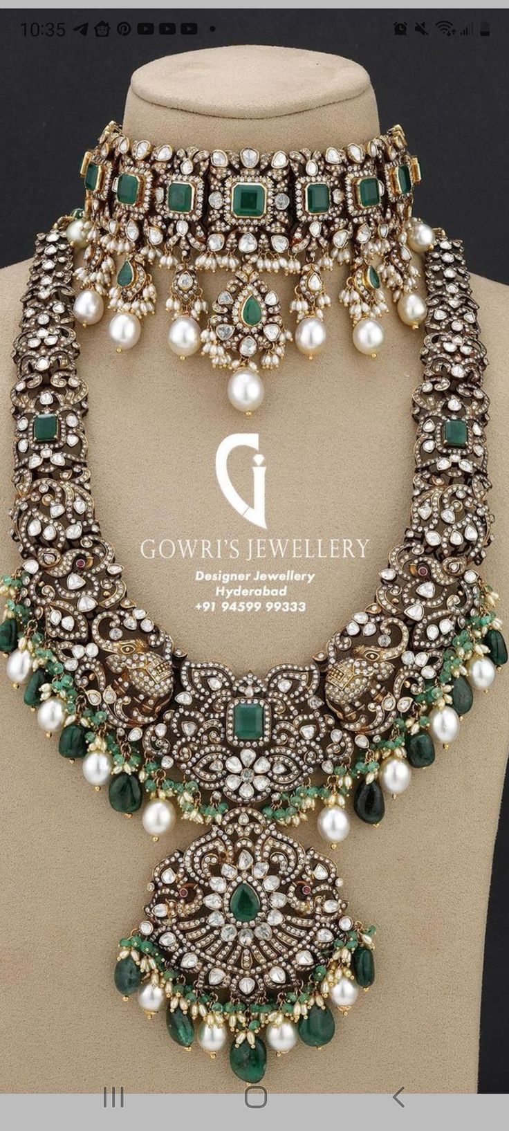 an elaborate necklace with pearls and emeralds on display in front of a mannequin