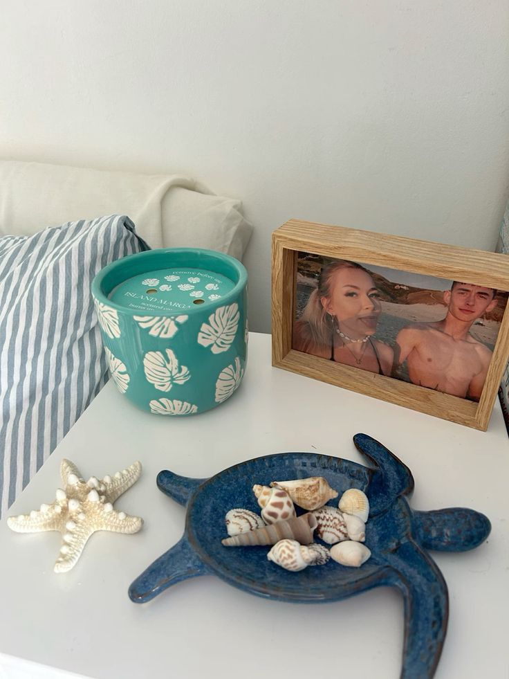 a table topped with shells and pictures next to a potted plant on top of a white table