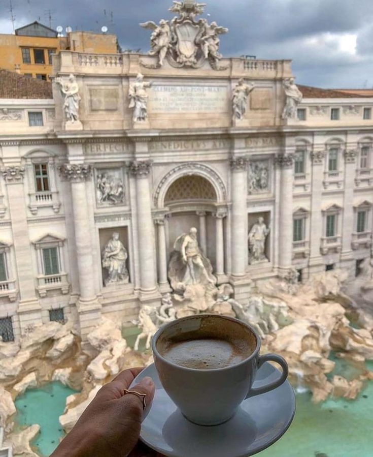 a cup of coffee on a saucer in front of a building with water fountain