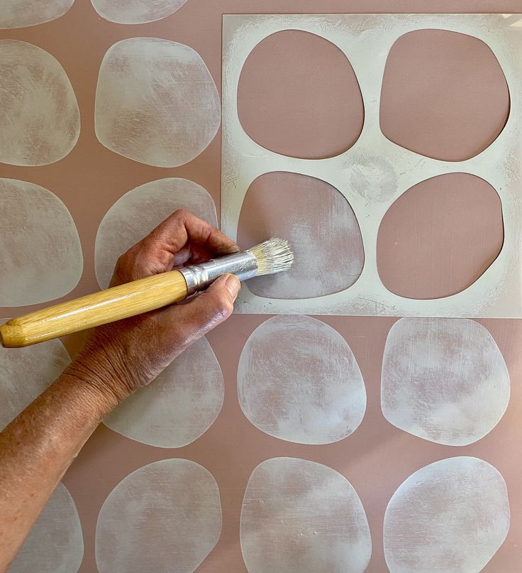 a person using a brush to paint circles on a wall with pink and white paper