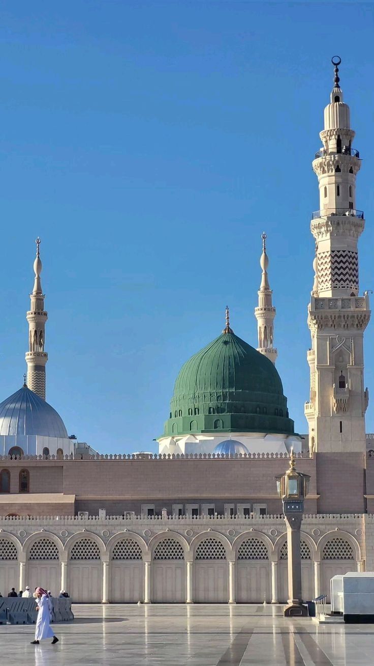 two people walking in front of a large building with green and white domes on it