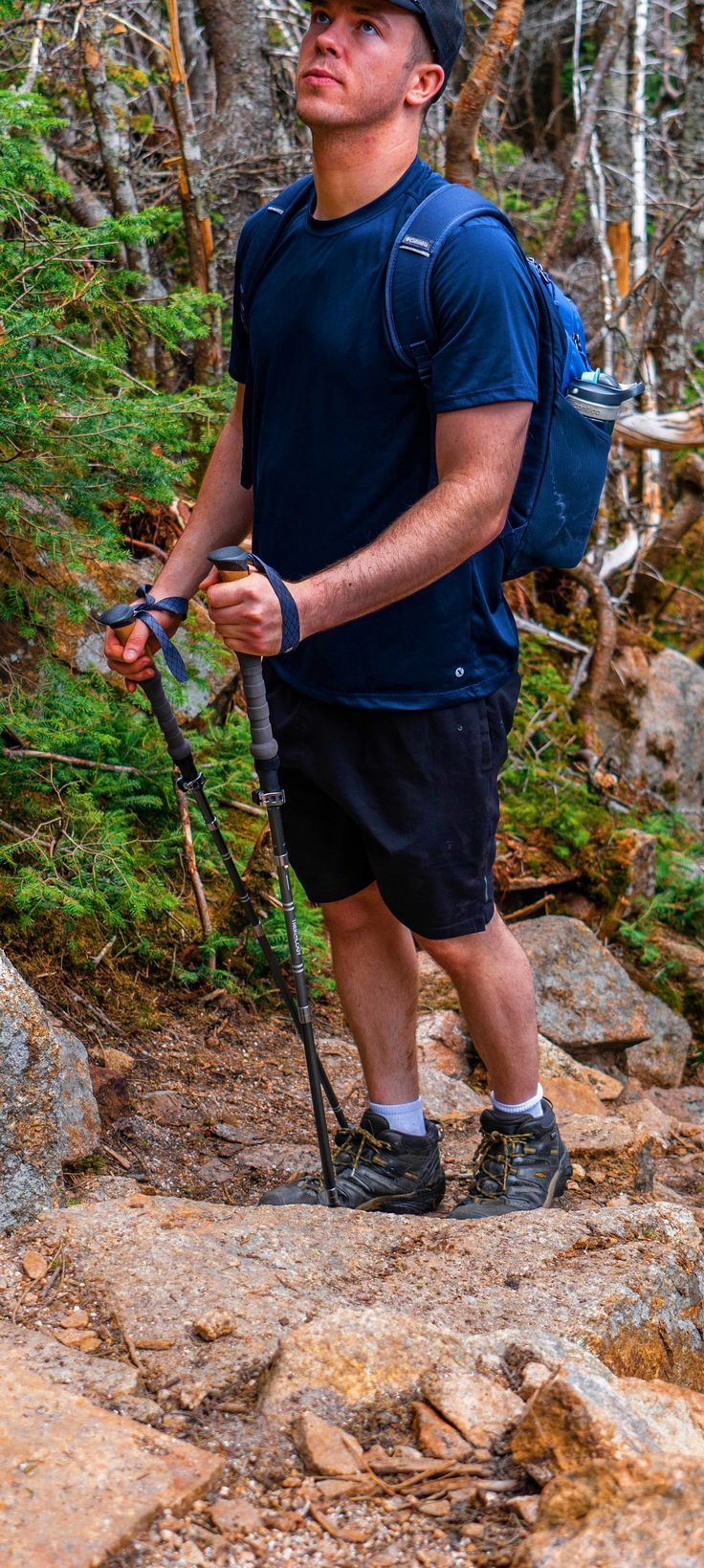 a man with a backpack and hiking poles on a rocky trail in the woods,