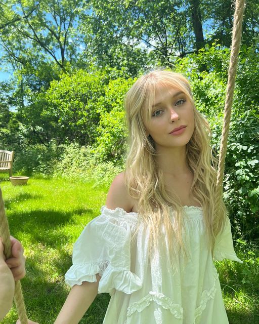 a woman in a white dress is on a swing with a cowboy hat and long blonde hair