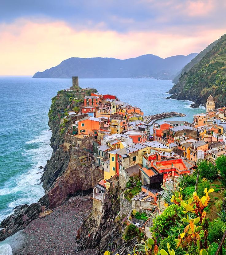 an aerial view of a village on the edge of a cliff overlooking the ocean with mountains in the background