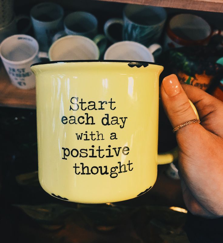 a hand holding a yellow coffee mug with words on it that read start each day with a positive thought