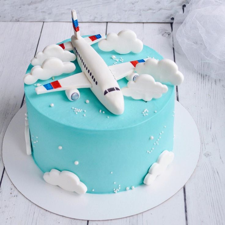 a blue cake with an airplane on top and clouds around it, sitting on a white plate