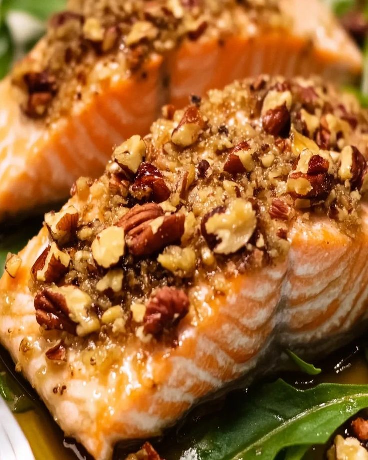 two salmon fillets with nuts on top of green leaves