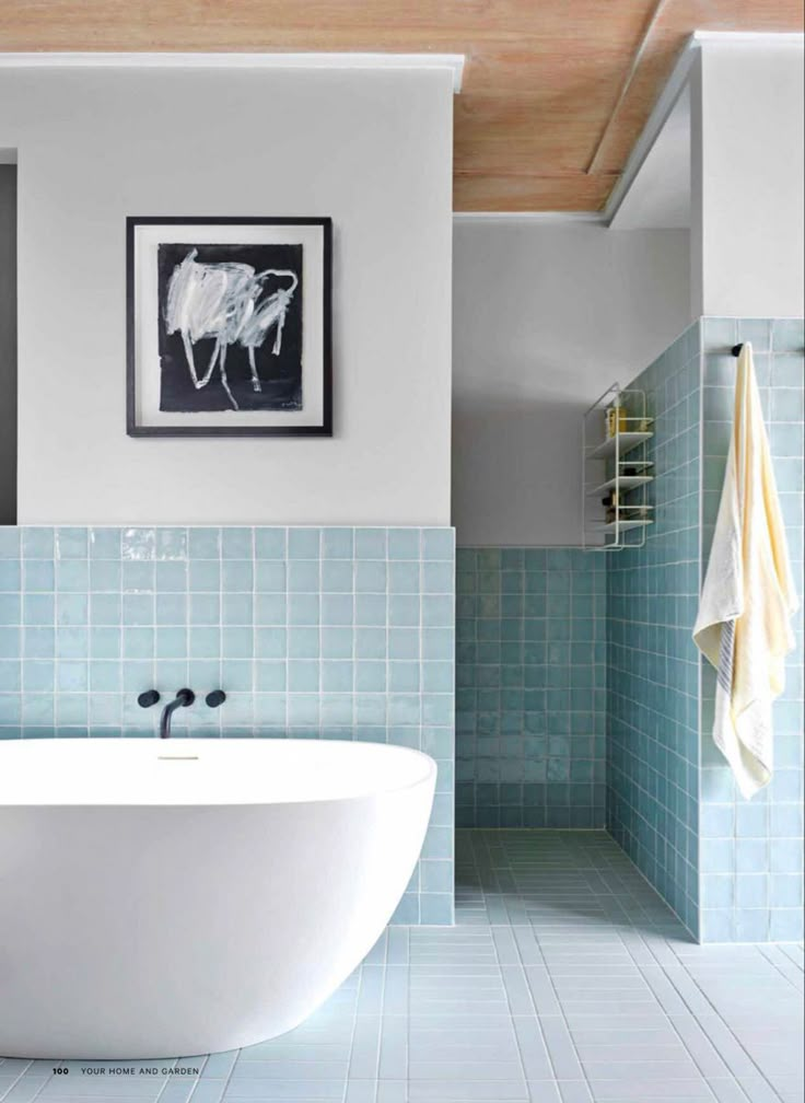 a white bath tub sitting next to a blue tiled wall in front of a painting