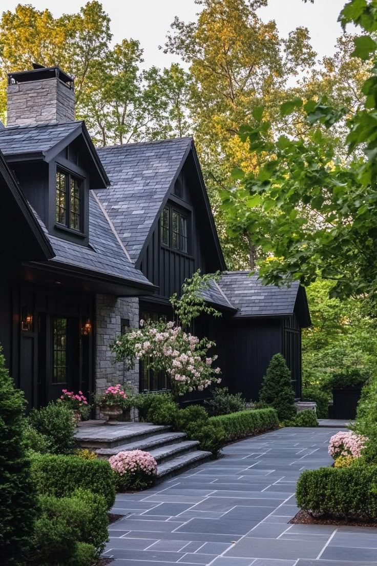 a black house surrounded by lush green trees and bushes with steps leading up to the front door