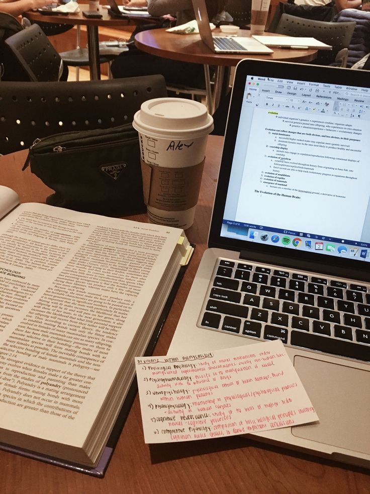 an open book sitting on top of a table next to a laptop computer and cup of coffee