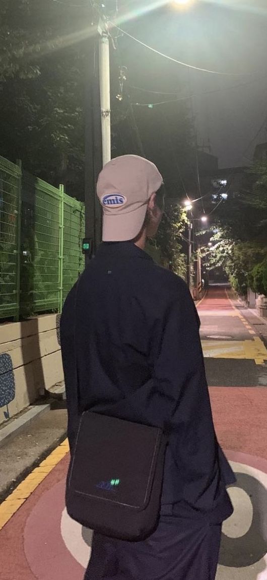 a man walking down the street at night with his back to the camera, carrying a black bag