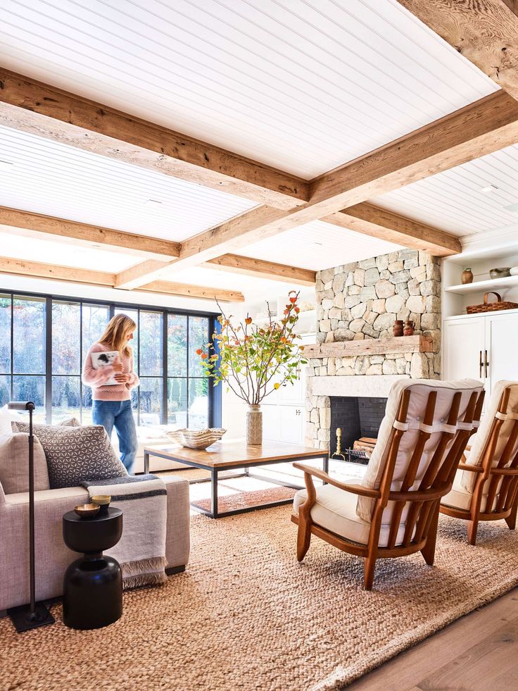 a woman standing in a living room next to a couch and chair with a fireplace