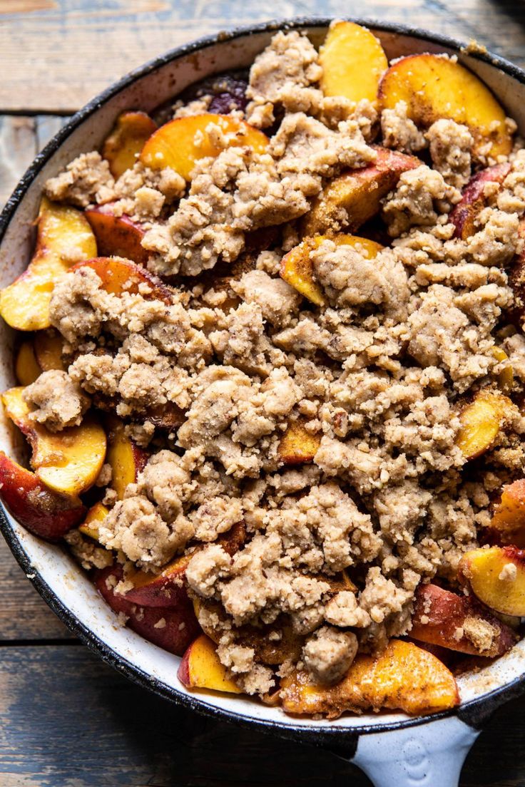 a skillet filled with meat and peaches on top of a wooden table