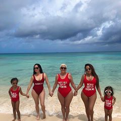 three women in red swimsuits holding hands while standing on the beach with two small children