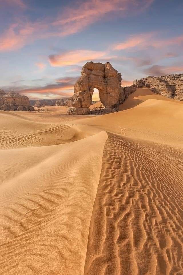 the desert is covered in sand and rocks, with an arch shaped like a rock