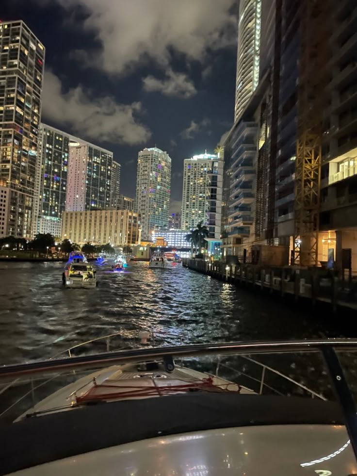 a boat traveling down a river in front of tall buildings at night with lights on