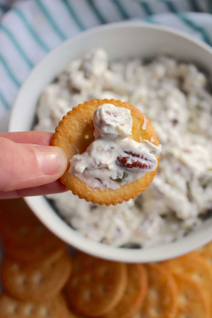 a hand holding a cracker over a bowl of dip