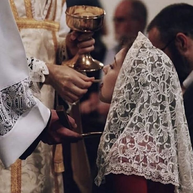 a priest is holding a small child's hand while other people stand in the background