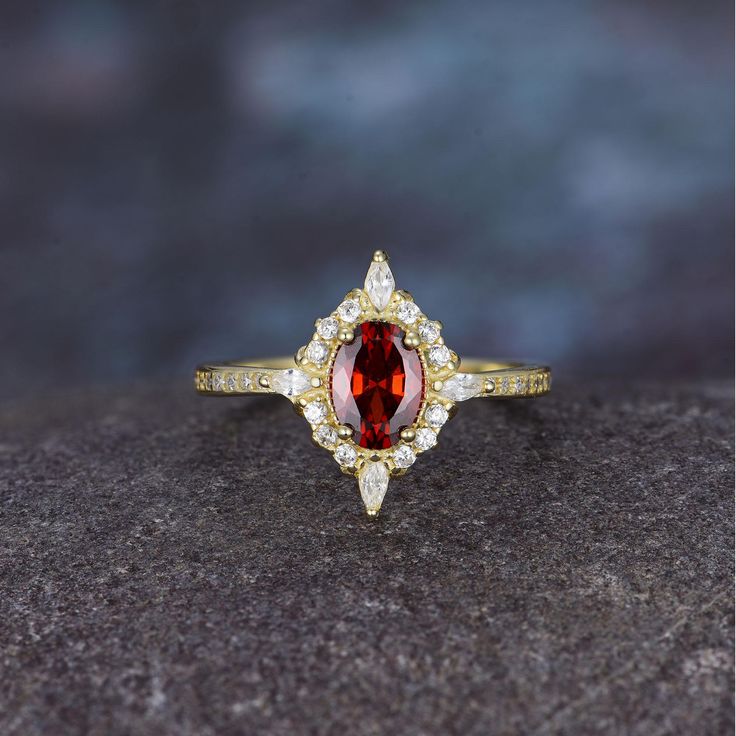 a red and white diamond ring sitting on top of a black stone surface with gold trimmings