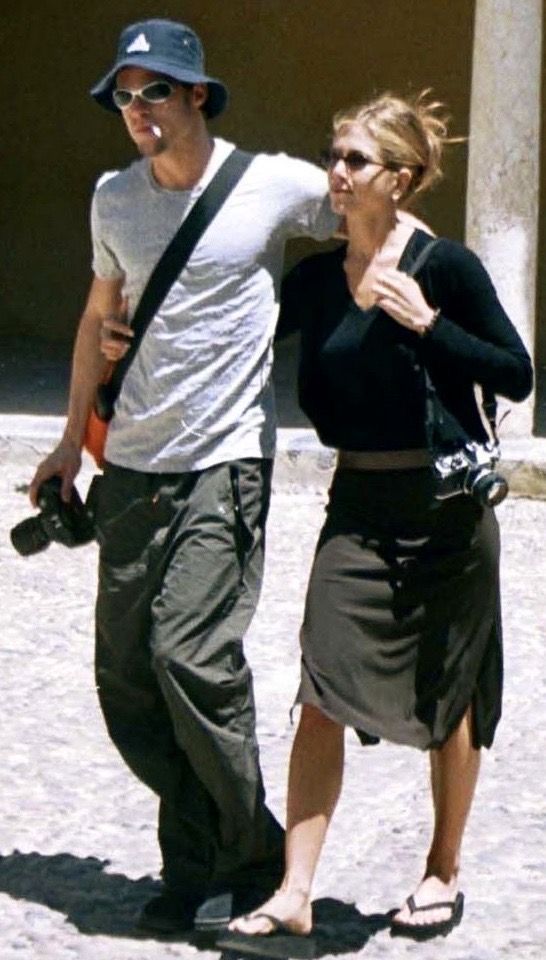 a man and woman are walking down the street with sunglasses on their heads, one is carrying a camera