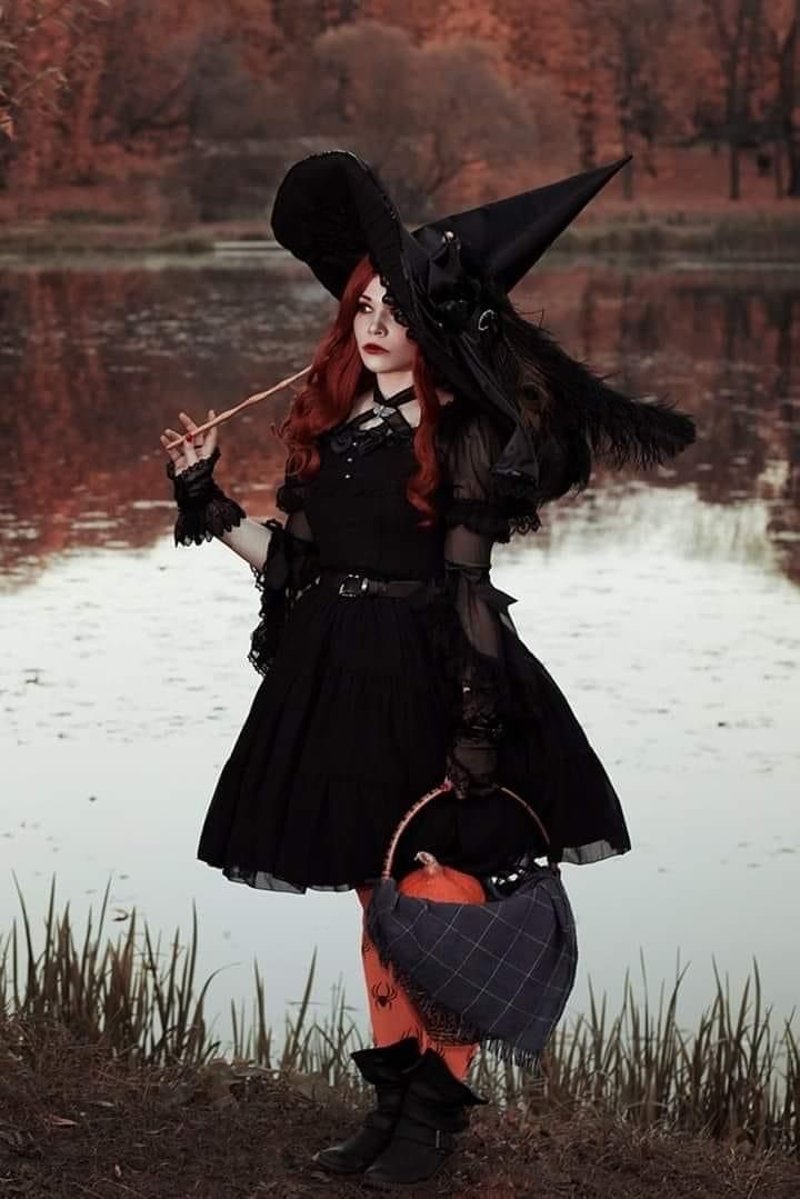 a woman with red hair wearing a black dress and witch hat holding a trick bag