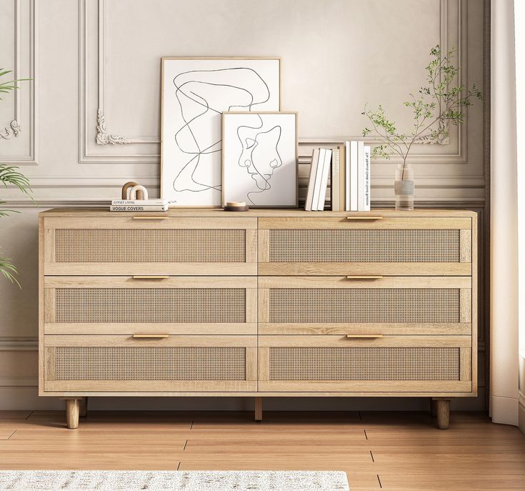 a wooden dresser sitting next to a plant and pictures on top of it in a living room