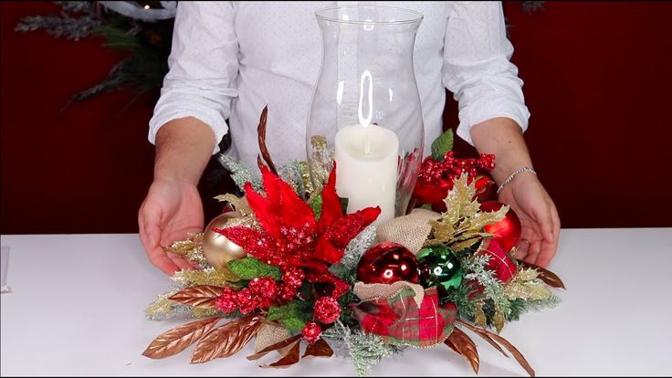 a person is holding a candle in front of some flowers and greenery on a table