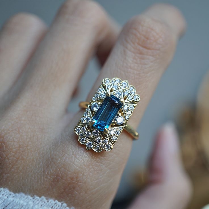 Read about our payment plans before proceeding. A ring that beautifully captures the ethereal allure of vintage design with a touch of celestial inspiration. This exquisite piece features a captivating emerald-cut London Blue Topaz at its center, radiating a deep, mesmerizing blue reminiscent of twilight skies. Surrounding the gemstone is a cluster of sparkling diamonds, each one set in a delicate, vintage-inspired gold setting that evokes the timeless beauty of heirloom jewelry. The intricate details of the gold filigree, combined with the serene blue of the topaz, create a sense of floating among the clouds, making this ring a perfect choice for those who dream of vintage charm with a modern twist. All orders come in our Tippy Taste ring box. This ring is handmade and designed in NYC. 14 Celestial Inspiration, Heirloom Rings, Heirloom Jewelry, Twilight Sky, Heirlooms Jewelry, Gold Filigree, London Blue Topaz, Blue Topaz Ring, London Blue