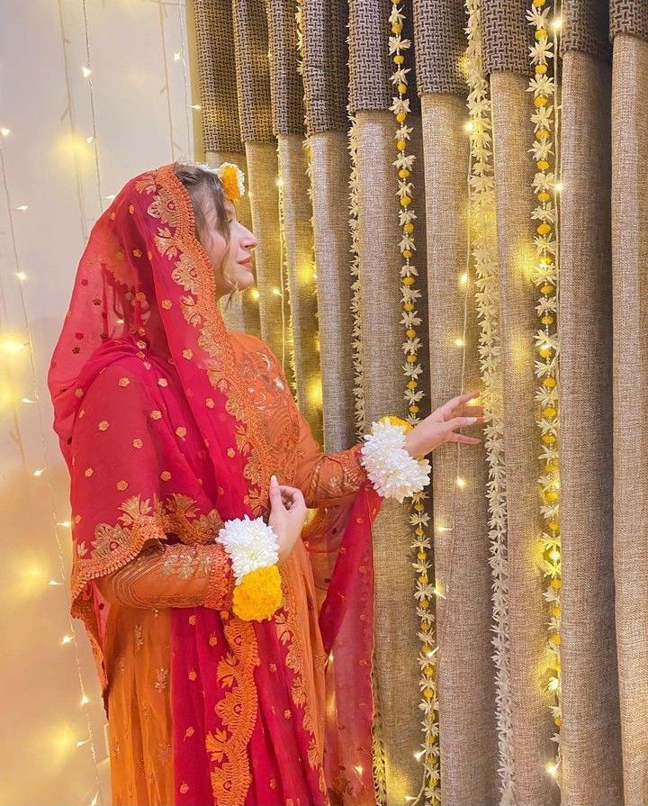 a woman in an orange and red outfit standing next to a curtain with lights on it