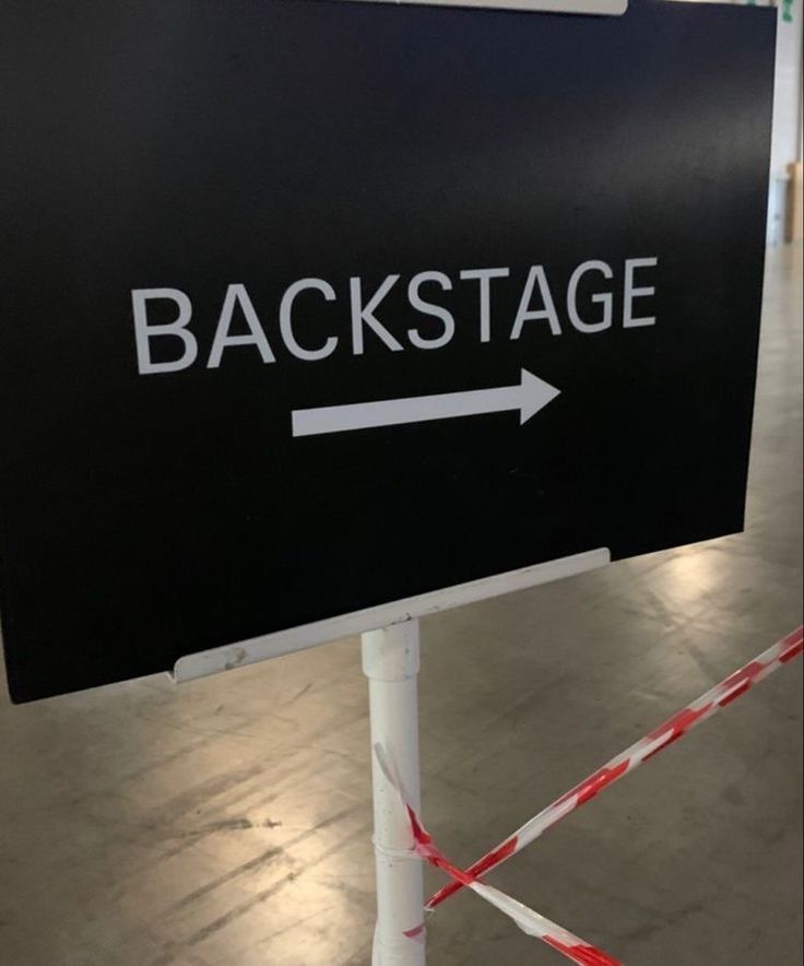 a black sign that says backstage with an arrow pointing to the back stage and red tape around it